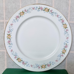Könnte beinhalten: Ein weißer Keramik-Dinnerteller mit goldfarbenem Rand und einem floralen Design in Rosa-, Gelb- und Blautönen.
