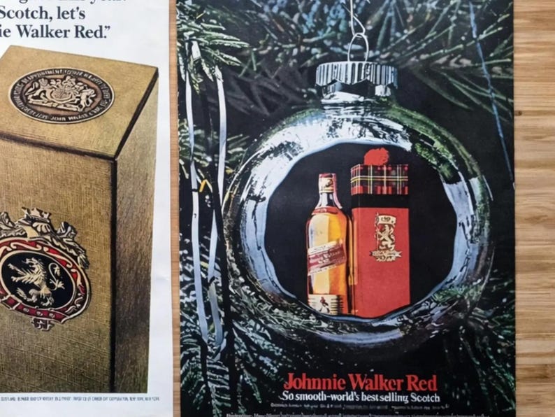 May include: An advertisement featuring a Johnnie Walker Red bottle and gift box inside a Christmas ornament. The bottle and box are red and gold, with the brand name prominently displayed. The background is a dark green with pine needles.