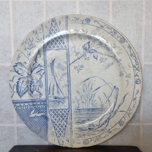 May include: A vintage blue and white ceramic plate with a floral design and a sailboat scene. The plate has a scalloped edge and a raised rim.