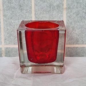 May include: A square glass vase with a clear outer layer and a red inner layer. The vase is made of glass and has a modern design.