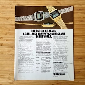 Puede incluir: Un anuncio con tres relojes digitales con correas metálicas. Los relojes son plateados y dorados, con pantallas digitales negras. El texto dice "OUR $69 SOLAR ALARM. A CHALLENGE TO EVERY CHRONOGRAPH IN THE WORLD."