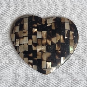 May include: Heart-shaped pendant with a mosaic design. The pendant is made of small, rectangular pieces in shades of brown, black, and cream. It has a small hole at the top for hanging. The mosaic pattern gives the pendant a textured appearance.