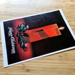 May include: A Christmas card with a festive design. The card features a red candle with a lit flame, holly with red berries, and the words "Happy Christmas" in white script. The background transitions from red to black.