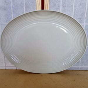 Puede incluir: Una fuente ovalada de color blanco roto con un borde acanalado. La fuente está hecha de cerámica y es adecuada para servir alimentos. El diseño es simple y elegante, lo que la convierte en una pieza versátil.