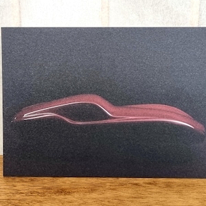 May include: A dark, textured card featuring a stylized, red outline of a car. The car's silhouette is depicted in a minimalist style, with a sleek, aerodynamic profile. The background is a deep, dark gray, creating a contrast with the red car.