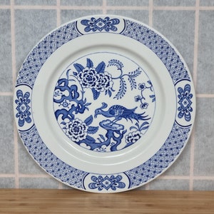 Może przedstawiać: Biały ceramiczny talerz obiadowy z niebiesko-białym wzorem kwiatowym. Wzór przedstawia ptaka, kwiaty i liście. Talerz ma niebiesko-biały brzeg.