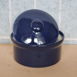 Könnte beinhalten: Eine dunkelblaue Keramikschale mit passendem Deckel. Die Schale hat eine abgerundete Form und eine glatte, glänzende Oberfläche.