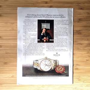 May include: An advertisement for a Rolex watch featuring a man in a suit and the text "Everything about David Plastow represents his company's philosophy. Which is why he wears a Rolex." The watch has a gold and silver band.