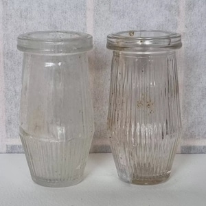 May include: Two clear glass jars with ribbed sides. The jars are empty and have a vintage look.