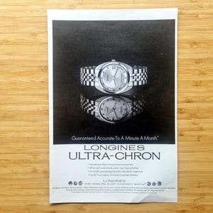 May include: Black and white advertisement for a Longines Ultra-Chron watch. The watch has a silver band and face. The text reads "Guaranteed Accurate To A Minute A Month".