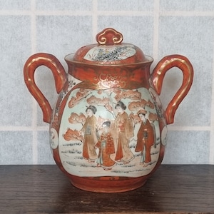 Peut inclure: Une théière en céramique rouge et blanche avec un couvercle et deux poignées. La théière est décorée d'une scène de femmes japonaises en vêtements traditionnels se promenant dans un jardin.