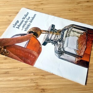 May include: An advertisement for Johnnie Walker whisky. The image shows a bottle of whisky being poured into a glass decanter. The text reads "a large Johnnie Walker...strictly for whisky drinkers."