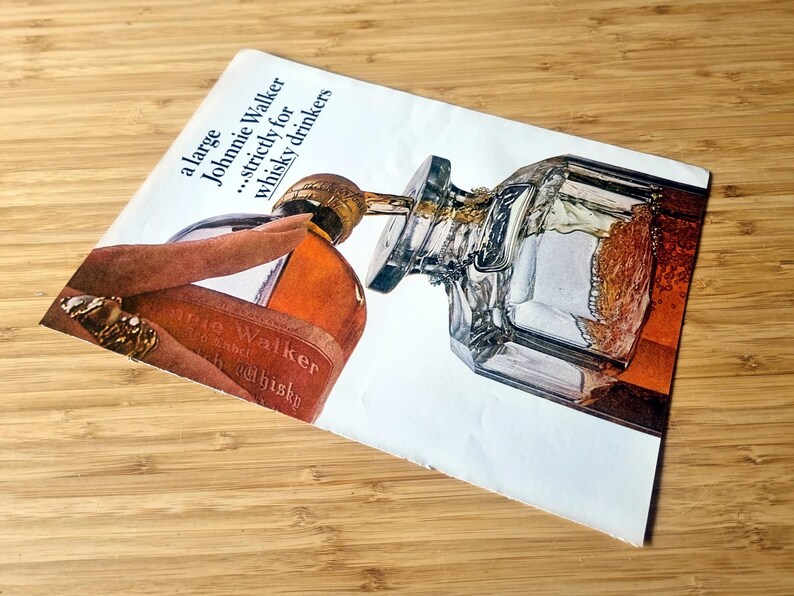 May include: An advertisement for Johnnie Walker whisky. The image shows a bottle of whisky being poured into a glass decanter. The text reads "a large Johnnie Walker...strictly for whisky drinkers."