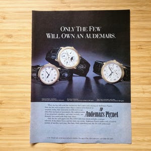 May include: An advertisement featuring three Audemars Piguet watches with black leather straps. The watches have gold-toned cases and white faces. The text reads "ONLY THE FEW WILL OWN AN AUDEMARS."