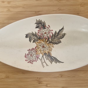 Könnte beinhalten: Weiße ovale Servierplatte aus Keramik mit einem Blumendesign mit gelben, rosa und braunen Chrysanthemen.