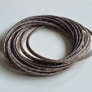May include: A stack of silver-coloured bangle bracelets with a textured surface.