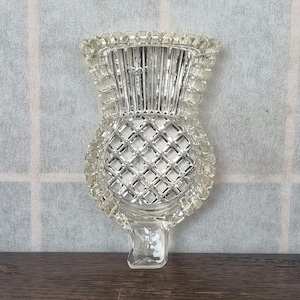 Puede incluir: Un plato de vidrio transparente con forma de cardo, con un patrón de diamante en la parte inferior y un borde texturizado.