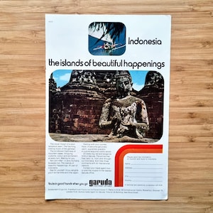 Könnte beinhalten: Vintage Reiseanzeige für Indonesien mit einem Foto einer sitzenden Statue vor einem Tempel. Die Anzeige enthält den Text "the islands of beautiful happenings" und das Garuda-Logo.