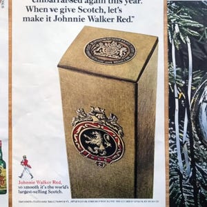 May include: Vintage advertisement featuring a tall, rectangular box of Johnnie Walker Red Scotch. The box is a light brown with ornate emblems and text. The ad also includes a bottle of J&B Scotch and the text "Johnnie Walker Red, so smooth it's the world's largest-selling Scotch."