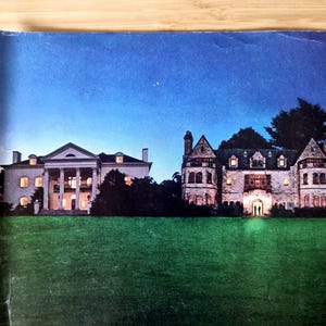 May include: An image of two illuminated mansions at dusk. The mansion on the left has a white facade with large columns. The mansion on the right is a stone structure with multiple turrets and lit windows. A green lawn is in the foreground.