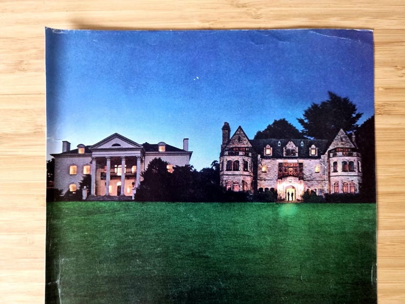 May include: An image of two illuminated mansions at dusk. The mansion on the left has a white facade with large columns. The mansion on the right is a stone structure with multiple turrets and lit windows. A green lawn is in the foreground.