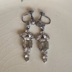 Può includere: Un paio di orecchini a clip argentati con un design pendente decorato con strass trasparenti.
