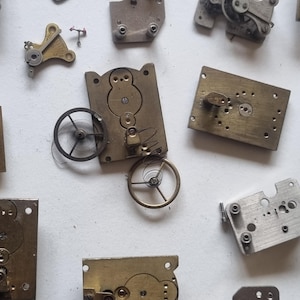May include: A collection of vintage watch parts, including gears, springs, and metal plates. The components are in various shapes and sizes, with a mix of brass and silver tones. The image showcases the intricate details of the disassembled watch mechanisms.