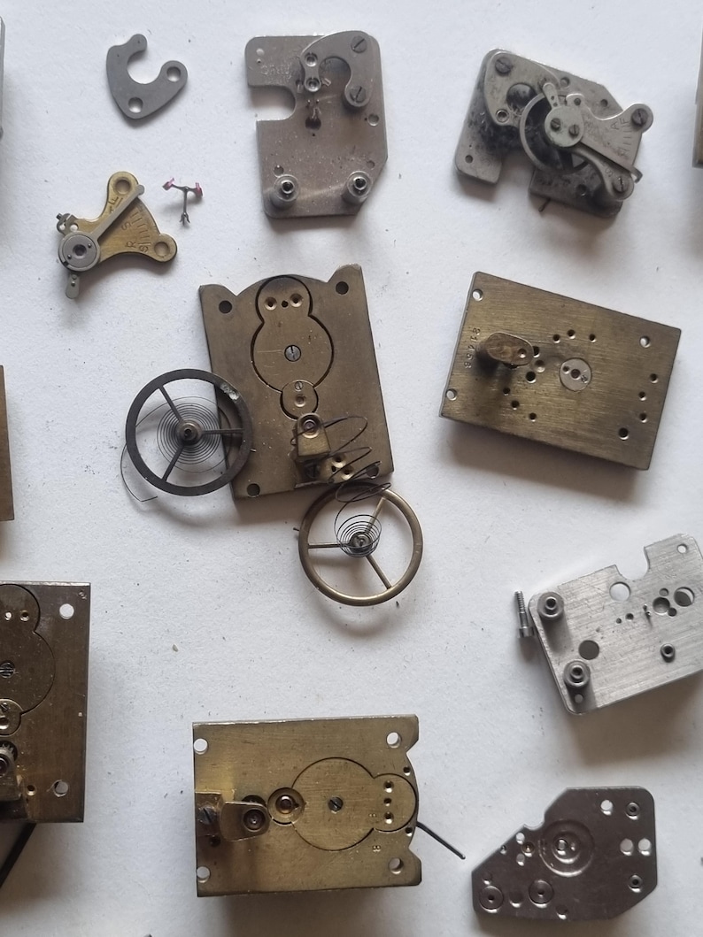 May include: A collection of vintage watch parts, including gears, springs, and metal plates. The components are in various shapes and sizes, with a mix of brass and silver tones. The image showcases the intricate details of the disassembled watch mechanisms.