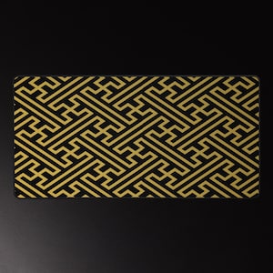 May include: A rectangular black desk mat featuring a repeating gold geometric pattern. The design consists of interlocking shapes, creating a visually complex and symmetrical arrangement. The mat has a smooth surface and a clean, modern aesthetic.