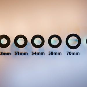 May include: A series of black circular lens filters, each with a different diameter, arranged horizontally. The sizes are labeled in millimeters: 35mm, 43mm, 51mm, 54mm, 58mm, 70mm, and 77mm. The background is a gradient of white and orange.