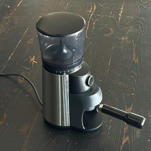 May include: A black and silver electric coffee grinder with a clear bean hopper and a black handle. The grinder has a dial for adjusting the grind size and is designed for home use.