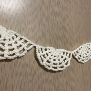 May include: A white crocheted garland with a scalloped design. The garland is made of delicate, intricate stitches and is perfect for adding a touch of elegance to any space.