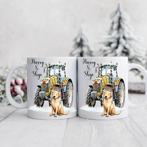 May include: Two white ceramic mugs with a festive design. Each mug features a yellow tractor decorated with lights, a golden Labrador, and the names "Harry & Skye" in elegant script. The mugs are set against a snowy backdrop.