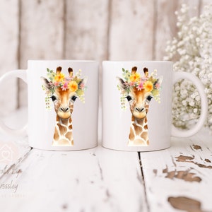 May include: Two white ceramic mugs with a watercolor illustration of a giraffe wearing a flower crown. The giraffe has a brown and tan spotted pattern. The mugs are on a white wooden surface.