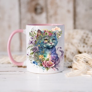 May include: A white ceramic mug with a pink rim and handle. The mug features a watercolor illustration of a blue cat with a flower crown, surrounded by colorful flowers and foliage.
