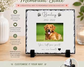 May include: A square natural slate plaque with rough-cut edges, displayed on two black plastic stands. The white surface features a printed photograph of a golden dog, the name Bailey, the dates 2012-2022, and the text You left paw prints on our hearts.