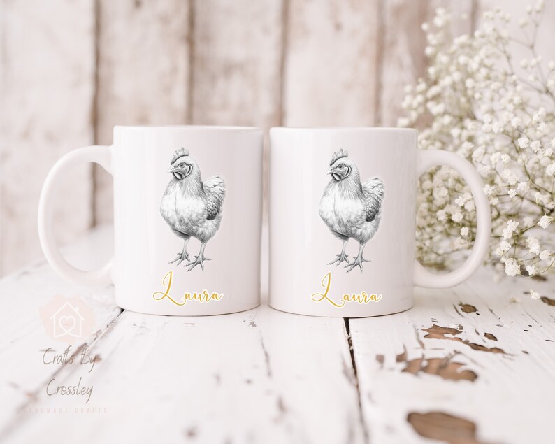 Op de afbeelding: Twee witte keramische mokken met een zwart-witte illustratie van een kip op elke mok. De mokken hebben de naam "Laura" in gouden letters op de bodem.