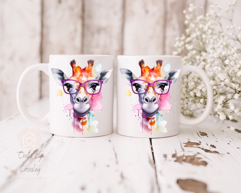 May include: Two white ceramic mugs with a watercolor giraffe design wearing purple glasses. The giraffe is surrounded by colorful watercolor splatters.