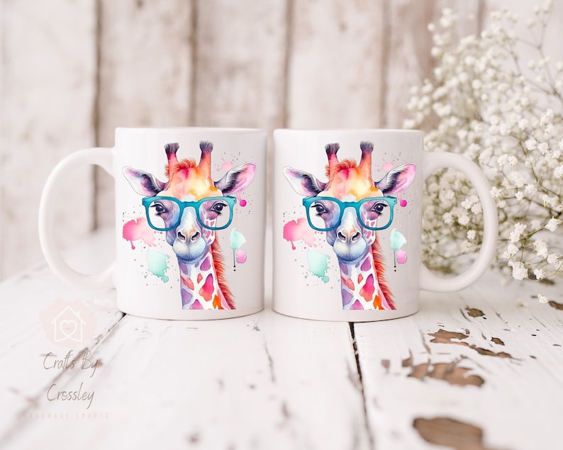 May include: Two white ceramic mugs with a watercolor illustration of a giraffe wearing blue glasses. The giraffe is surrounded by colorful watercolor splatters.