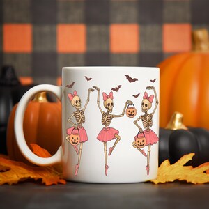 Pu&ograve; includere: Tazza in ceramica bianca con un design a tema Halloween. Il design presenta tre ballerine scheletro con tut&ugrave; e fiocchi rosa, che tengono lanterne a forma di zucca, circondate da pipistrelli. La tazza &egrave; ambientata su uno sfondo di zucche e foglie autunnali.