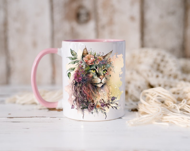 May include: A white ceramic mug with a pink rim and handle. The mug features a watercolor illustration of a cat wearing a flower crown. The cat has green eyes and brown fur. The background is a watercolor wash of yellow and pink.