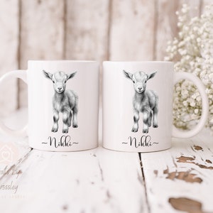May include: Two white ceramic mugs with black handles. Each mug features a black and white illustration of a baby goat and the name "Nikki" written below the image.