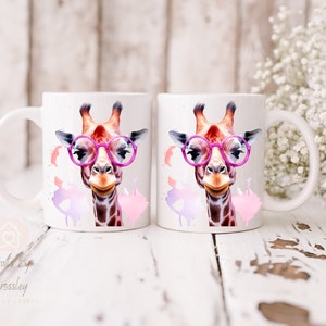 May include: Two white ceramic mugs with a colorful giraffe wearing pink glasses and pink watercolor splatters on each mug.