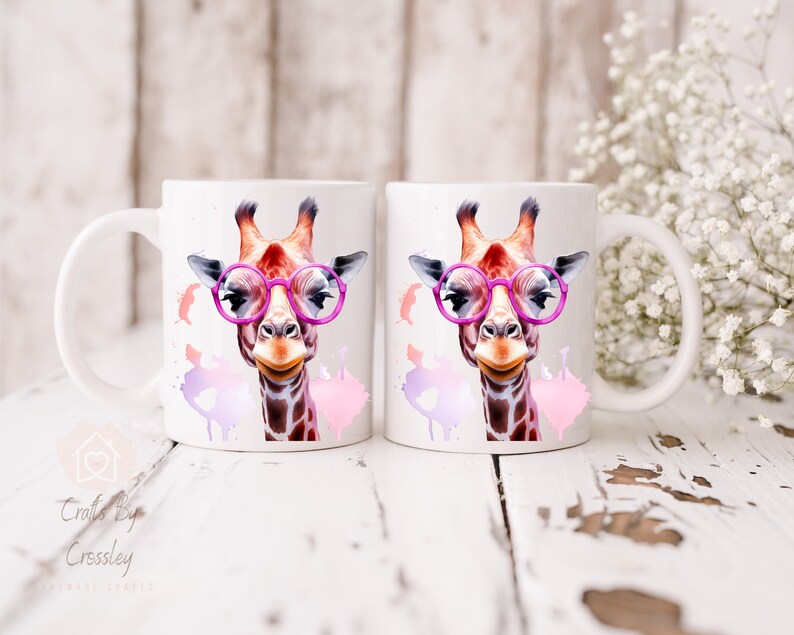May include: Two white ceramic mugs with a colorful giraffe wearing pink glasses and pink watercolor splatters on each mug.