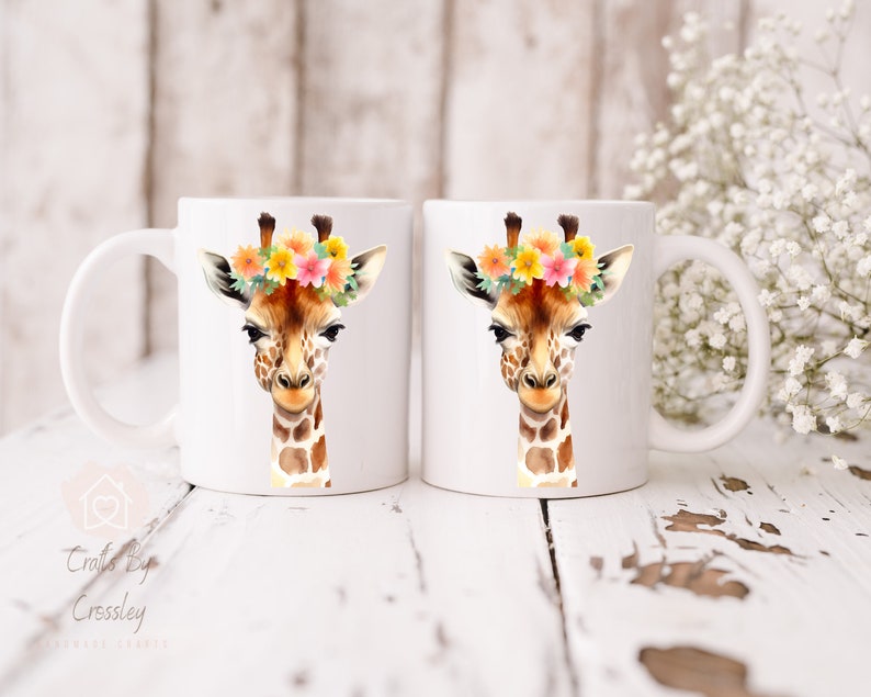 May include: Two white ceramic mugs with a giraffe wearing a floral crown printed on them. The giraffe has brown spots and a light brown face. The flowers are yellow, pink, and orange.