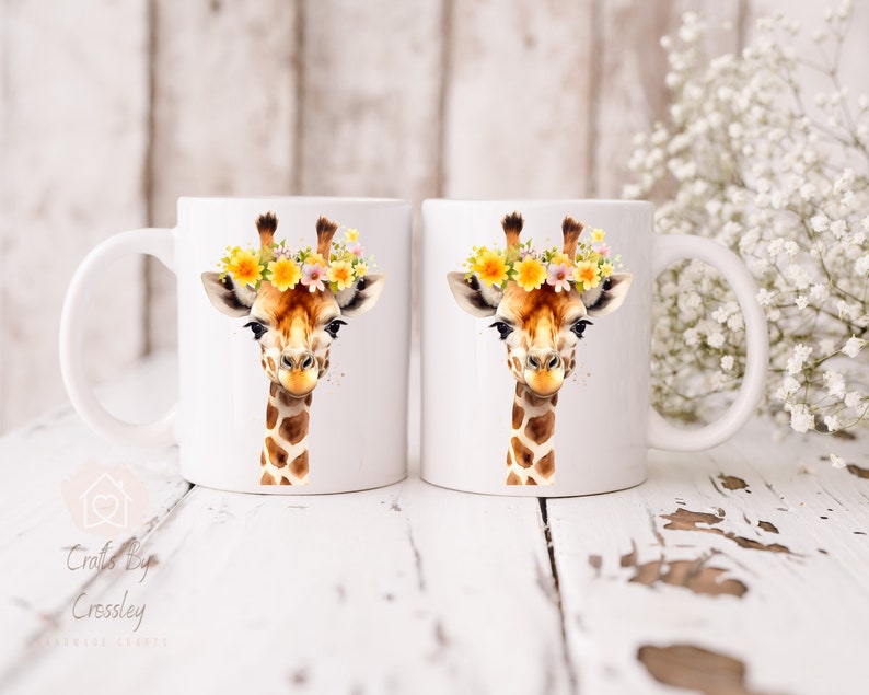 May include: Two white ceramic mugs with a watercolor illustration of a giraffe wearing a flower crown. The giraffe has brown spots and a light brown face. The mugs are on a white wooden surface.