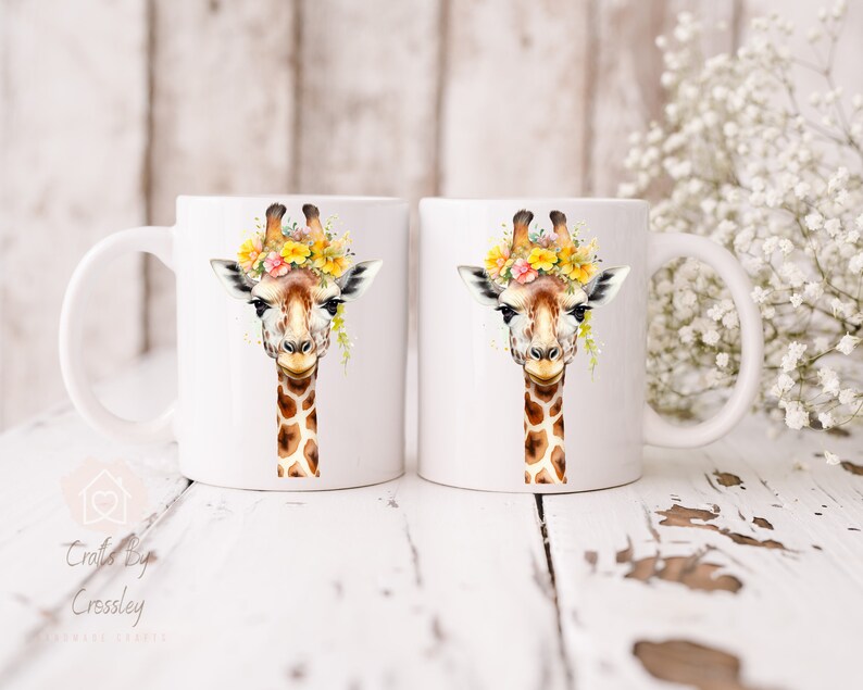 May include: Two white ceramic mugs with a giraffe wearing a flower crown printed on them. The giraffe has brown spots and a yellow flower crown.