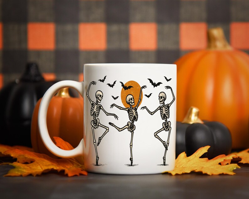 Pu&ograve; includere: Tazza in ceramica bianca con un design di Halloween con tre scheletri danzanti, pipistrelli e una luna piena. La tazza &egrave; ambientata su uno sfondo di zucche e foglie autunnali.