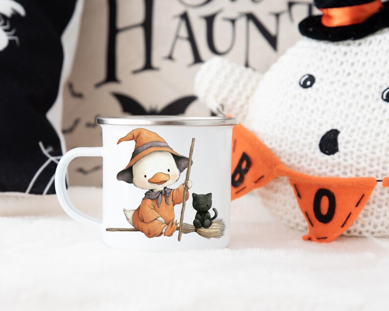 May include: White enamel mug featuring a cartoon duck dressed as a witch, wearing an orange hat and holding a broom. A black cat sits on the broom. Halloween-themed design. The mug has a silver rim and a white handle.