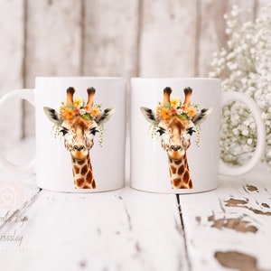 May include: Two white ceramic mugs with a giraffe wearing a flower crown printed on them. The giraffe has brown spots and a light brown face. The mugs are on a white wooden surface.